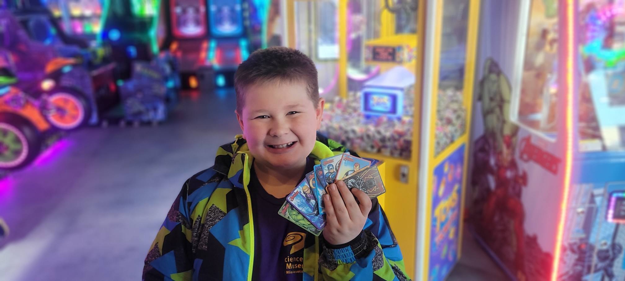 A young boy smiles while holding Marvel-themed arcade prize cards.