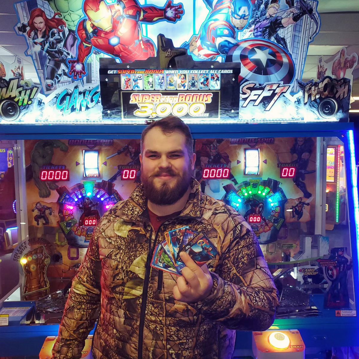 A player stands in front of a brightly lit Marvel Avengers arcade game.