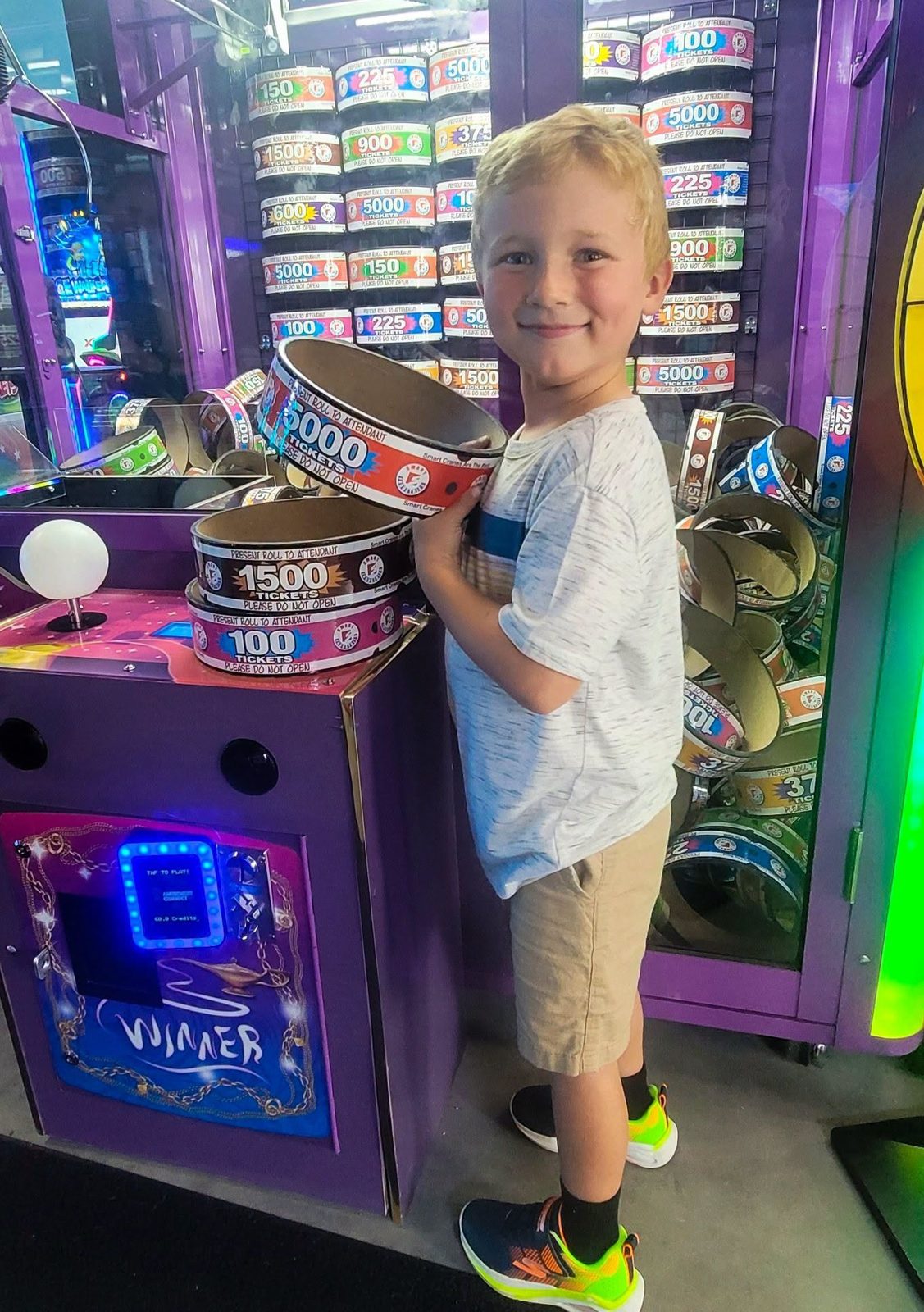 A boy grins with his arms full of ticket rings beside a jackpot game