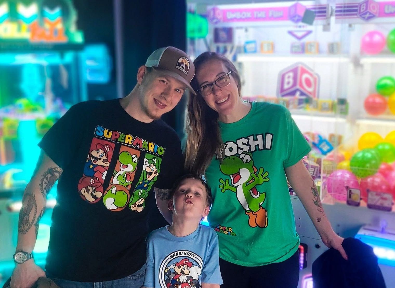 A family in matching Mario shirts smiles in front of the claw machines