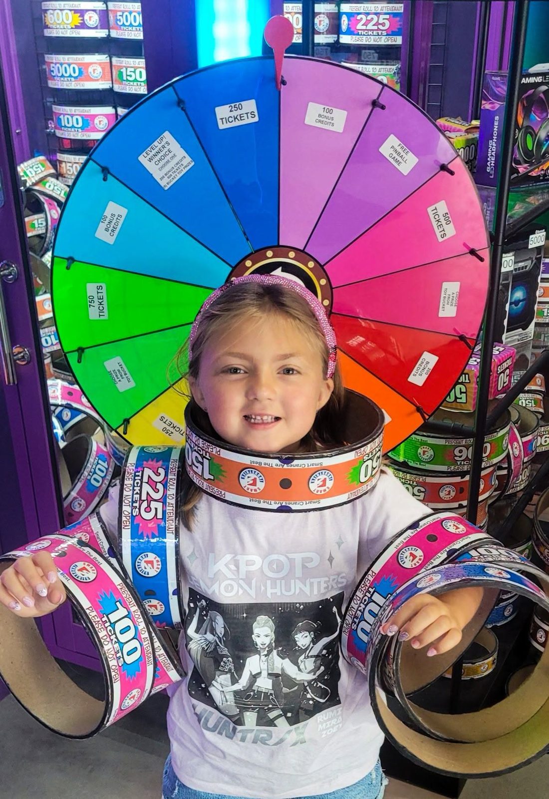 A girl wears ticket rings around her neck and arms in front of the prize wheel